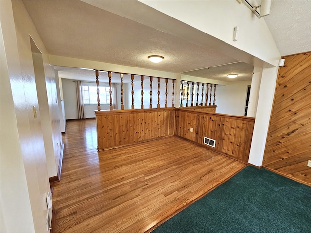 empty room with hardwood / wood-style floors, a textured ceiling, wooden walls, and vaulted ceiling