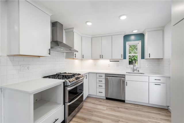 kitchen featuring white cabinetry, sink, stainless steel appliances, wall chimney range hood, and light hardwood / wood-style flooring