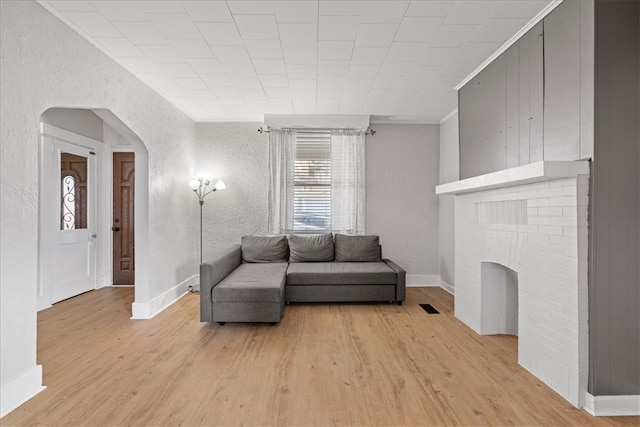 living room with a brick fireplace, light hardwood / wood-style flooring, and ornamental molding