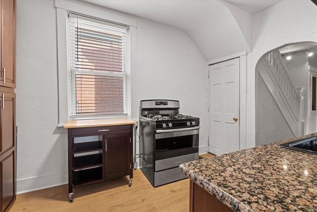 kitchen with stainless steel gas range oven, dark stone countertops, light wood-type flooring, and vaulted ceiling