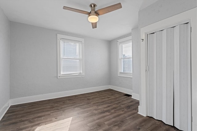 unfurnished bedroom with a closet, dark hardwood / wood-style floors, multiple windows, and ceiling fan