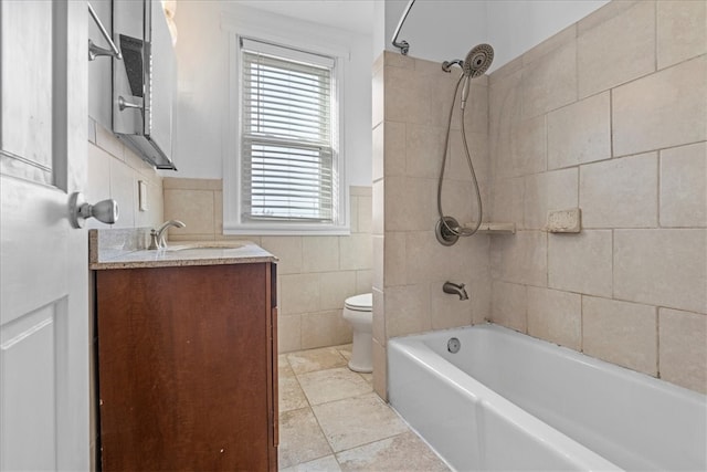 full bathroom with vanity, toilet, tiled shower / bath, and tile walls