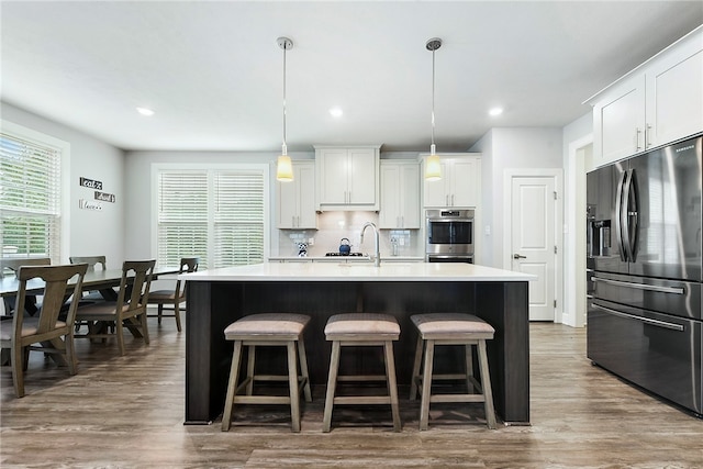 kitchen with stainless steel appliances, dark hardwood / wood-style flooring, pendant lighting, a kitchen island with sink, and white cabinets