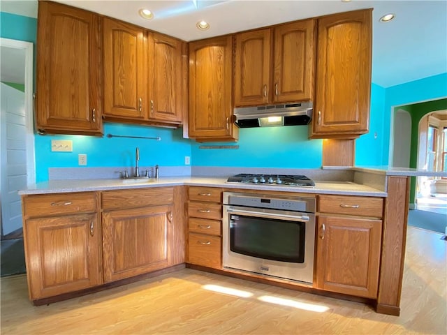 kitchen with kitchen peninsula, sink, stainless steel appliances, and light wood-type flooring