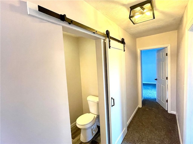 hall with dark colored carpet and a barn door