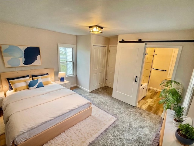 bedroom with a barn door, light hardwood / wood-style floors, and ensuite bath