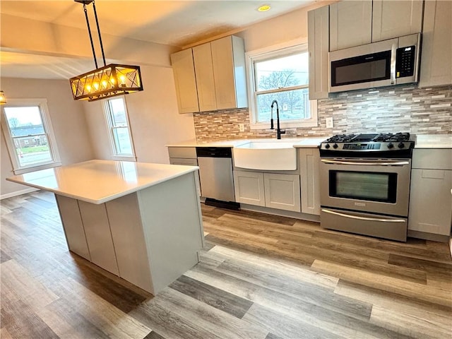 kitchen with pendant lighting, sink, light hardwood / wood-style flooring, appliances with stainless steel finishes, and a kitchen island