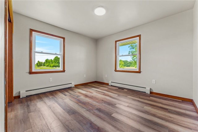 empty room with a healthy amount of sunlight, a baseboard radiator, and light hardwood / wood-style floors