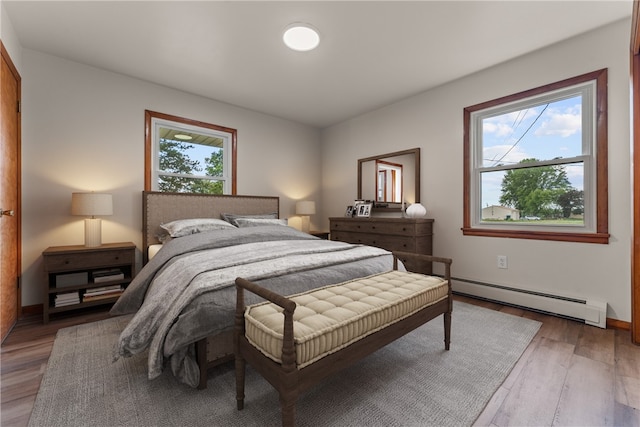 bedroom featuring hardwood / wood-style flooring, multiple windows, and a baseboard heating unit