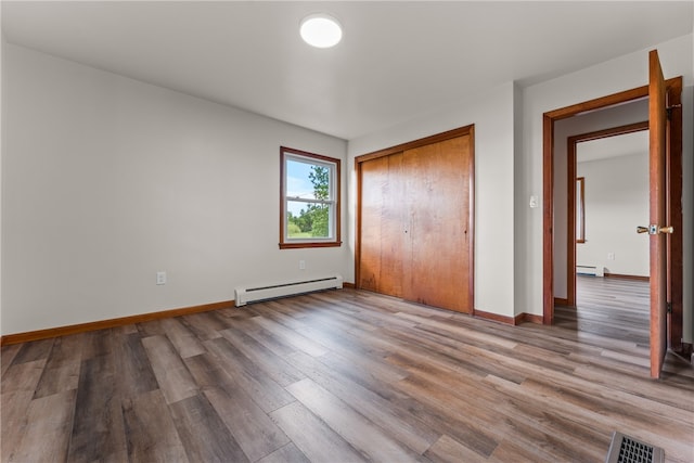 unfurnished bedroom with hardwood / wood-style floors, a closet, and a baseboard radiator