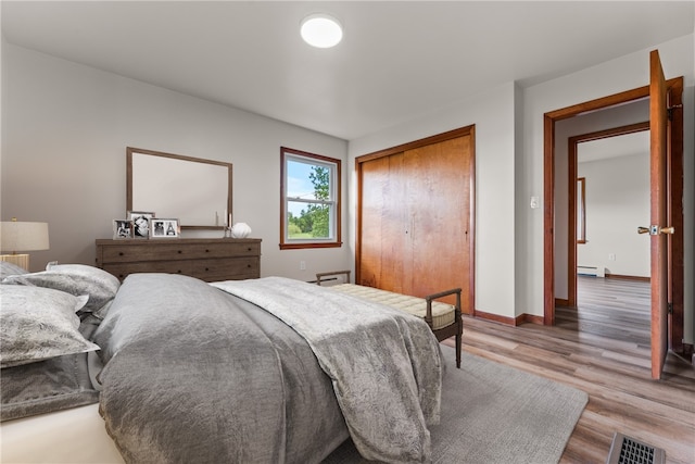 bedroom with hardwood / wood-style floors, a baseboard radiator, and a closet