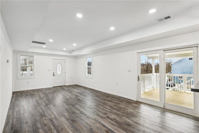 unfurnished living room featuring dark wood-type flooring, a raised ceiling, and a healthy amount of sunlight