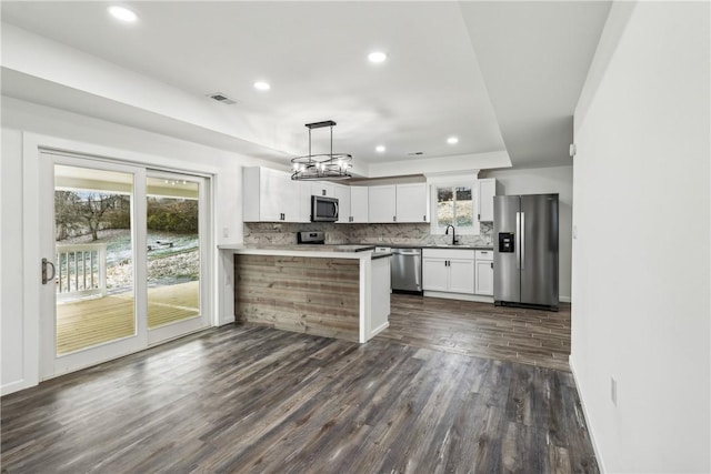 kitchen with kitchen peninsula, dark hardwood / wood-style flooring, stainless steel appliances, pendant lighting, and white cabinetry