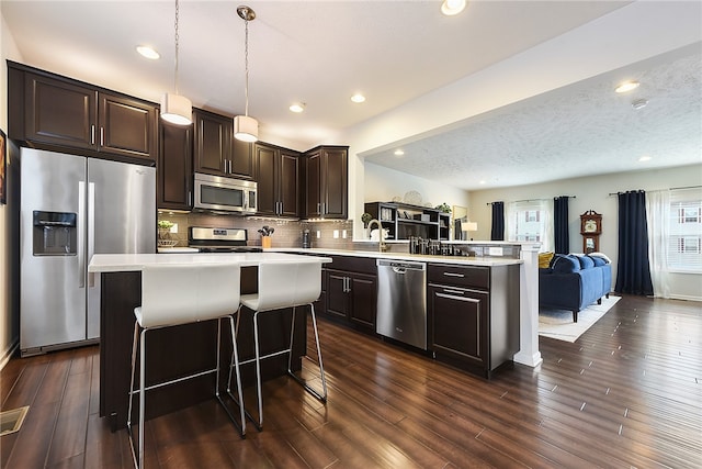 kitchen with stainless steel appliances, dark hardwood / wood-style floors, pendant lighting, a textured ceiling, and decorative backsplash