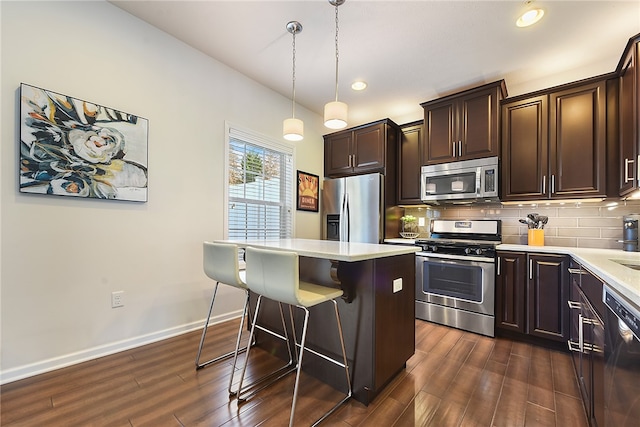 kitchen featuring appliances with stainless steel finishes, a kitchen breakfast bar, dark wood-type flooring, decorative light fixtures, and a kitchen island