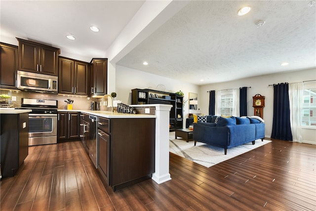 kitchen with kitchen peninsula, decorative backsplash, dark hardwood / wood-style flooring, a textured ceiling, and stainless steel appliances