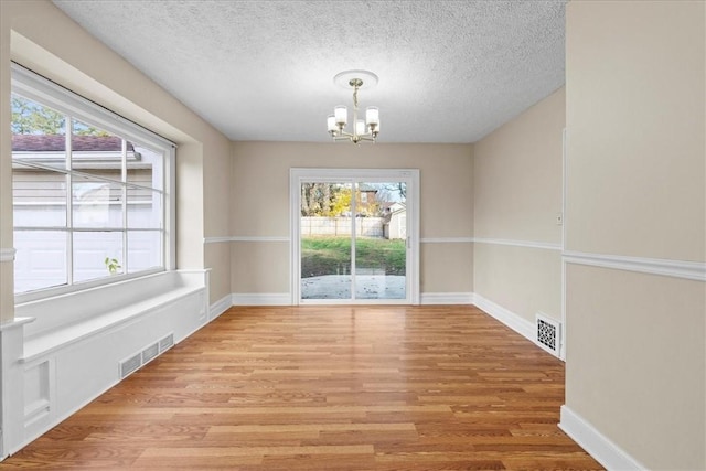 unfurnished dining area featuring plenty of natural light, light hardwood / wood-style floors, a textured ceiling, and a chandelier