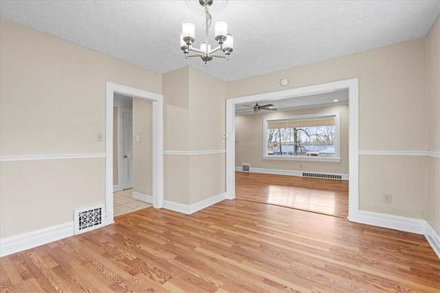 unfurnished dining area featuring light hardwood / wood-style flooring, ceiling fan with notable chandelier, and a textured ceiling