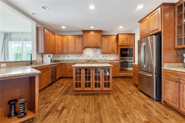 kitchen with appliances with stainless steel finishes, light hardwood / wood-style floors, light stone counters, and sink