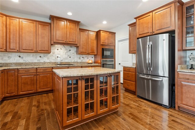 kitchen with a center island, light stone countertops, tasteful backsplash, dark hardwood / wood-style flooring, and stainless steel appliances