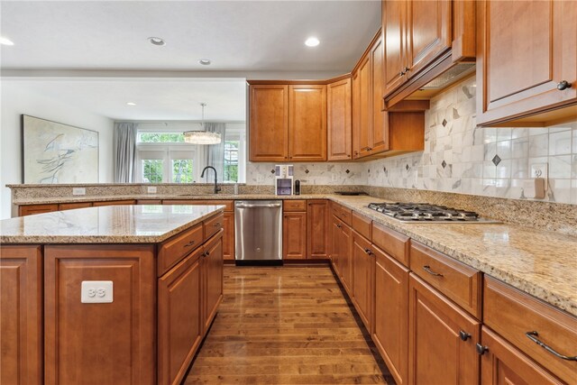 kitchen featuring light stone countertops, a center island, hanging light fixtures, stainless steel appliances, and hardwood / wood-style flooring