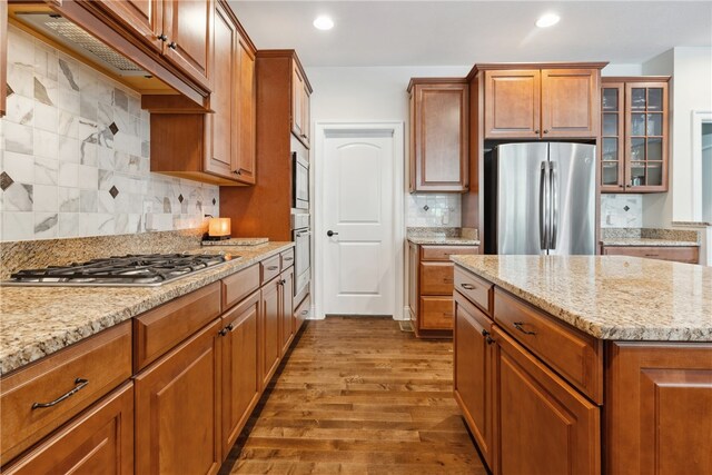 kitchen featuring hardwood / wood-style flooring, light stone countertops, appliances with stainless steel finishes, and tasteful backsplash