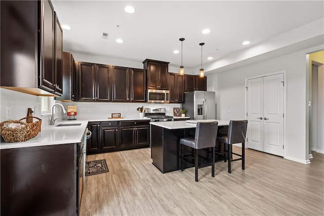 kitchen featuring a center island, sink, hanging light fixtures, stainless steel appliances, and a breakfast bar