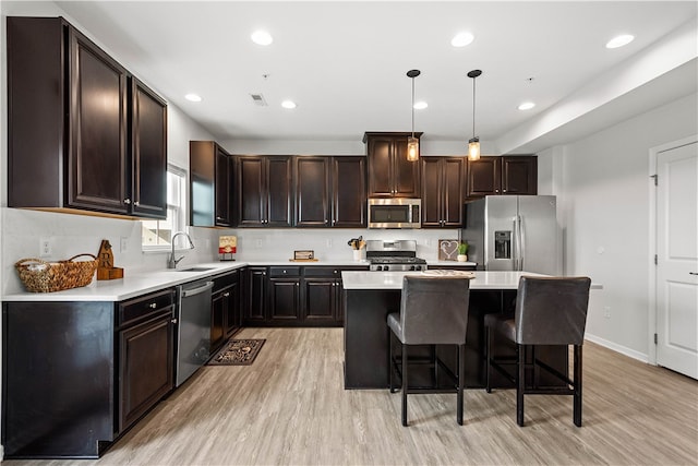 kitchen with sink, hanging light fixtures, light hardwood / wood-style flooring, appliances with stainless steel finishes, and a kitchen island