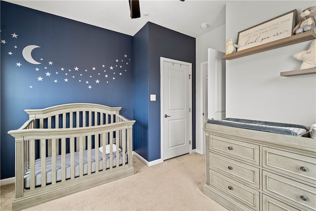 bedroom featuring ceiling fan, a nursery area, and light carpet