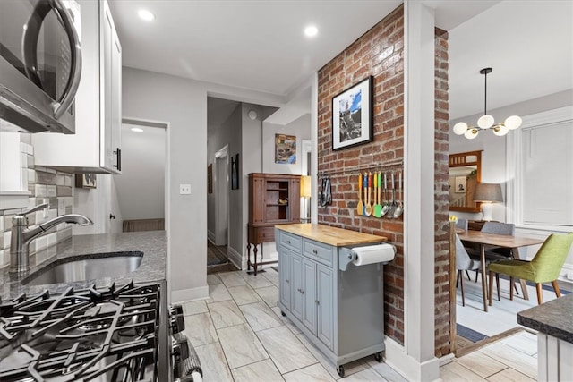 kitchen featuring pendant lighting, wood counters, white cabinets, sink, and a notable chandelier