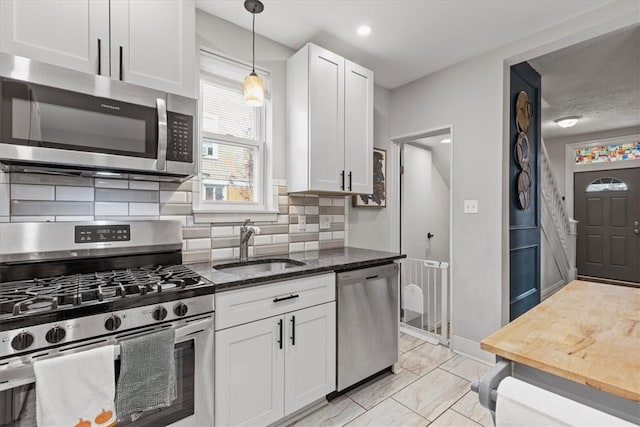 kitchen featuring appliances with stainless steel finishes, tasteful backsplash, sink, dark stone countertops, and white cabinetry