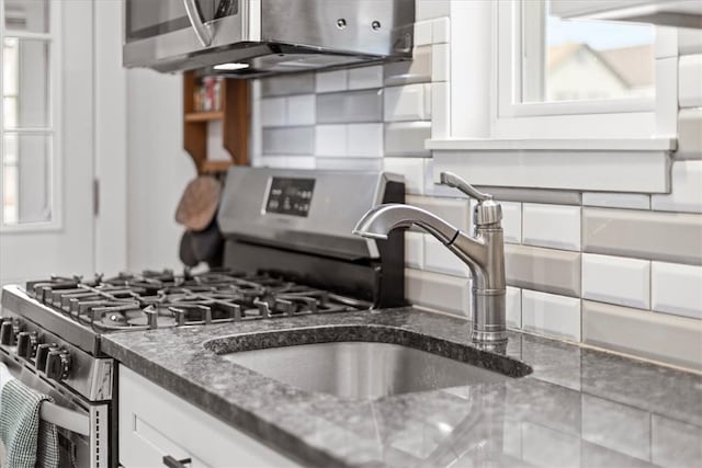 kitchen featuring tasteful backsplash, white cabinetry, stainless steel range with gas cooktop, and dark stone counters