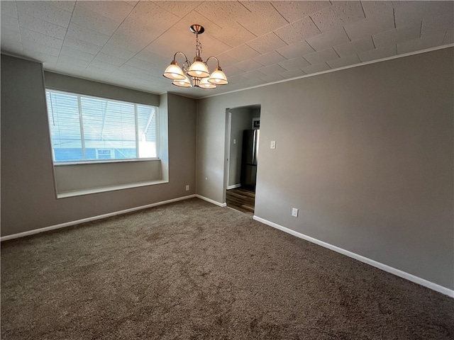 empty room with an inviting chandelier, ornamental molding, and dark colored carpet