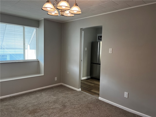 unfurnished room featuring a notable chandelier, dark carpet, and ornamental molding