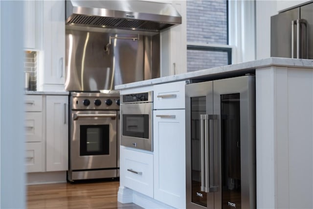 kitchen with high quality appliances, light hardwood / wood-style flooring, white cabinets, and ventilation hood