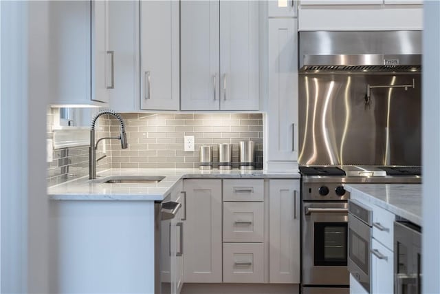 kitchen featuring white cabinets, sink, light stone countertops, stainless steel range, and tasteful backsplash