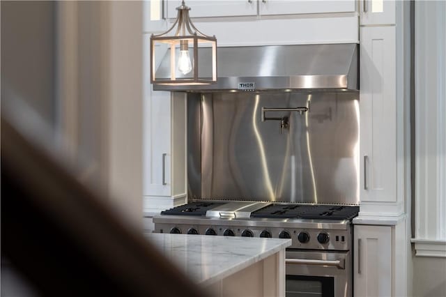 kitchen featuring white cabinetry, light stone countertops, wall chimney exhaust hood, pendant lighting, and stainless steel stove