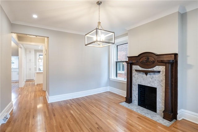 unfurnished living room with a tiled fireplace, crown molding, light hardwood / wood-style flooring, and a chandelier