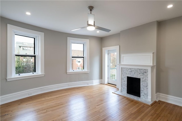 unfurnished living room featuring light wood-type flooring, a stone fireplace, plenty of natural light, and ceiling fan