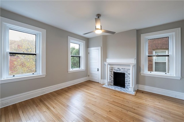 unfurnished living room with ceiling fan, light wood-type flooring, and a tiled fireplace