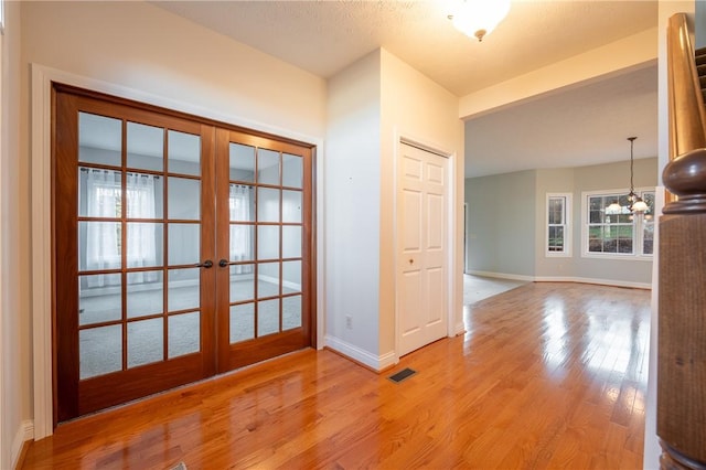 interior space with a textured ceiling, a chandelier, light hardwood / wood-style flooring, and french doors