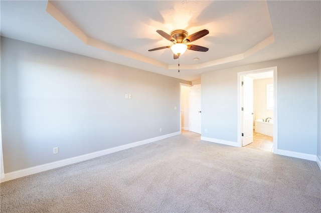 unfurnished bedroom featuring a tray ceiling, connected bathroom, ceiling fan, and light carpet