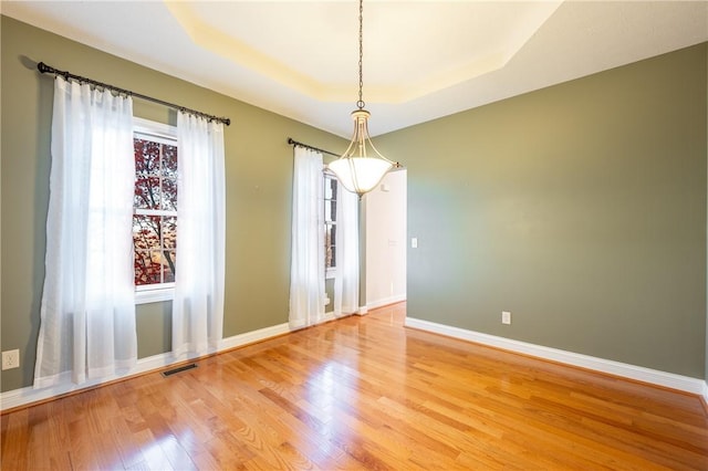 empty room with hardwood / wood-style floors and a tray ceiling