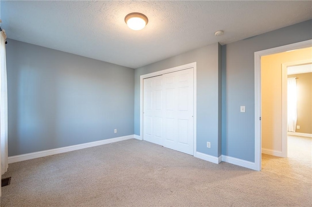 unfurnished bedroom featuring a textured ceiling, light carpet, and a closet