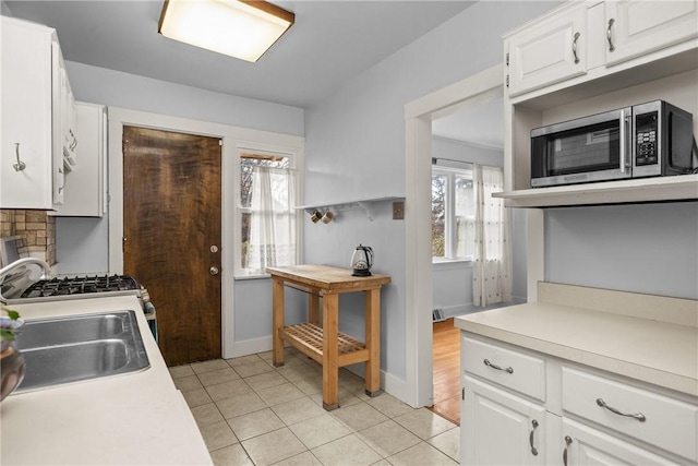 kitchen with decorative backsplash, sink, white stove, white cabinetry, and light tile patterned flooring