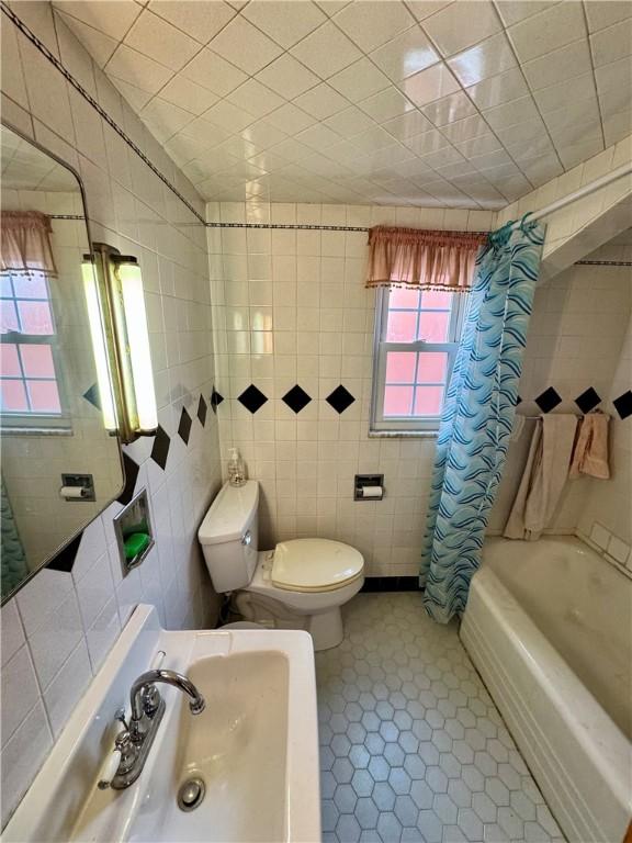 bathroom featuring tile patterned flooring, toilet, tile walls, and shower / tub combo