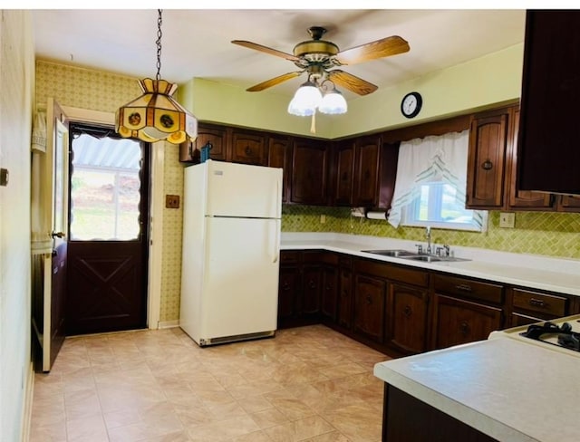 kitchen with white refrigerator, sink, hanging light fixtures, tasteful backsplash, and dark brown cabinets