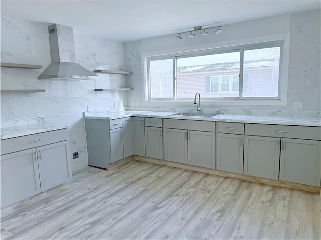 kitchen with wall chimney exhaust hood, plenty of natural light, sink, and light hardwood / wood-style flooring