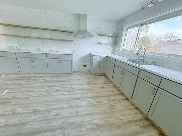 kitchen with gray cabinets, sink, wall chimney exhaust hood, and light wood-type flooring