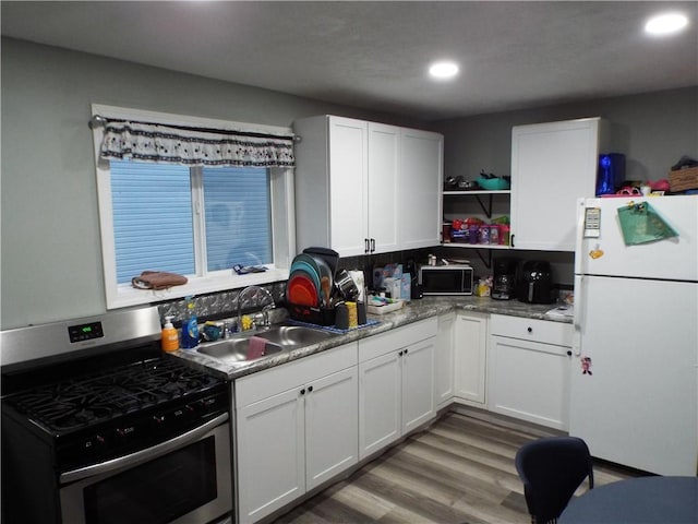 kitchen featuring light wood-type flooring, stainless steel gas range, sink, white cabinets, and white fridge